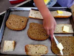 En una charola para hornear, colocar las rebanadas de pan. Untar la mantequilla a cada pieza de pan y por ultimo agregar el azúcar.